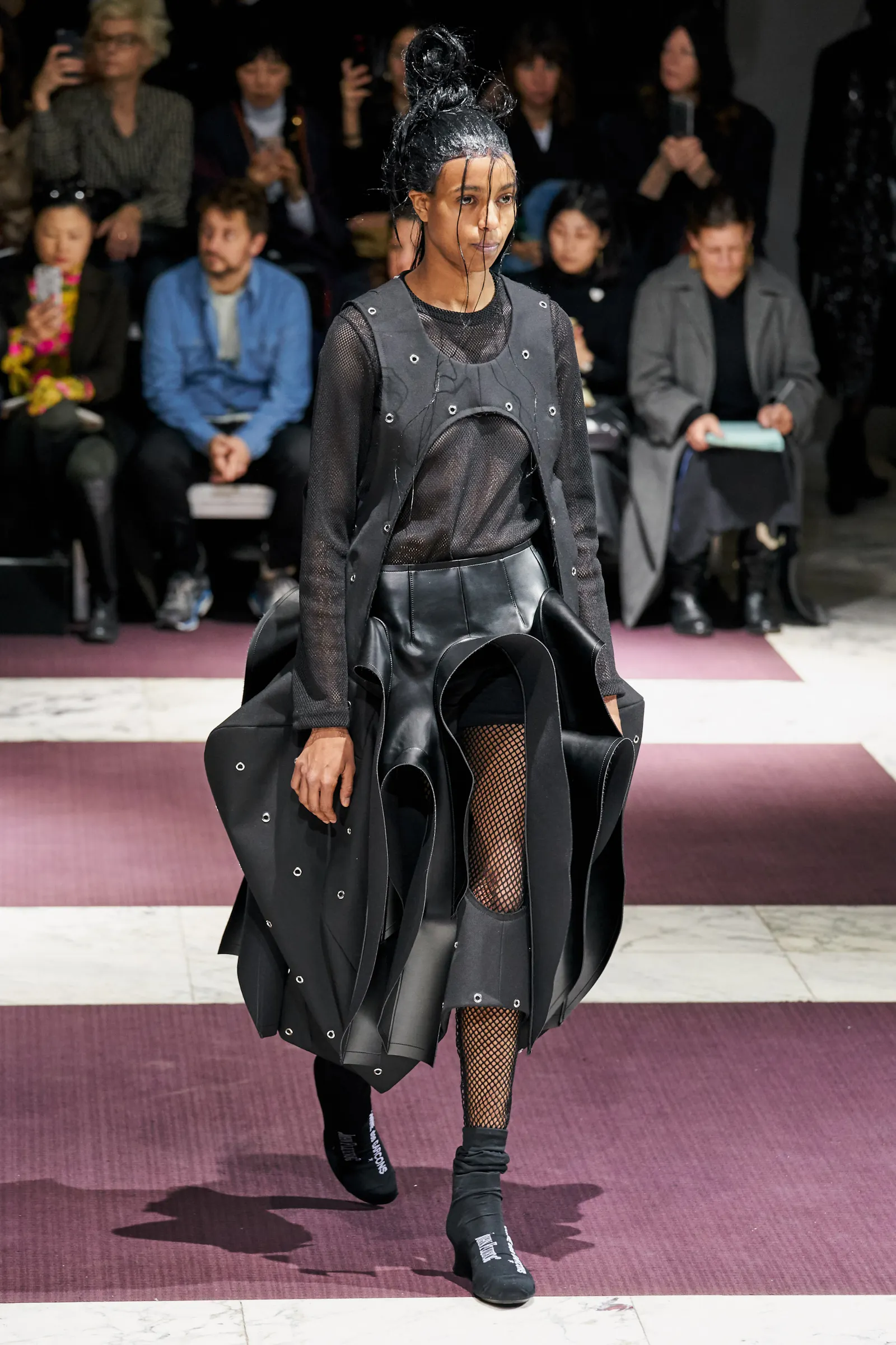 Model, das ein schwarzes Outfit mit vielen Schichten auf dem Laufsteg trägt.