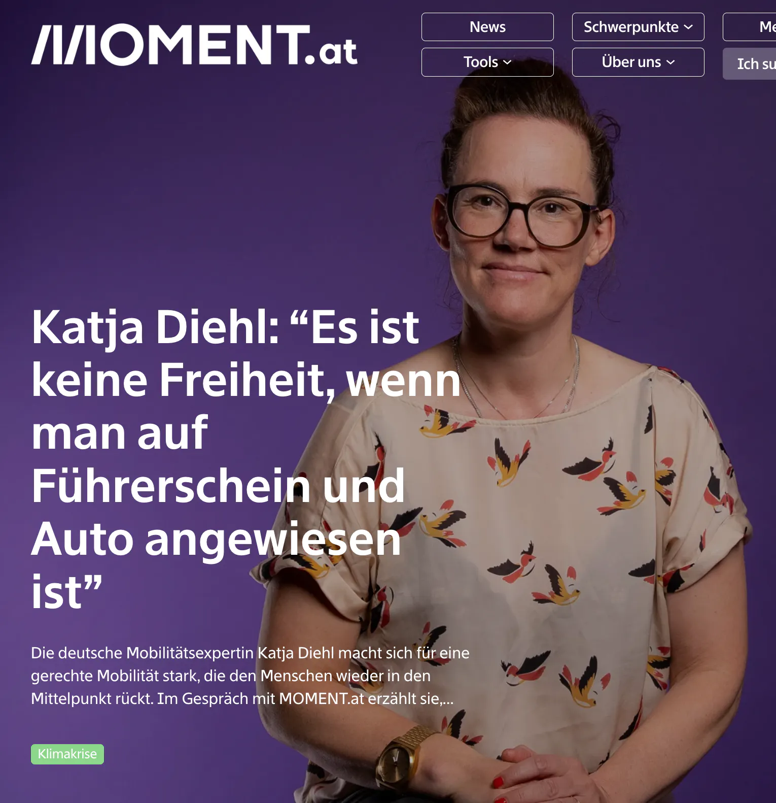 Screenshot eines Artikels von MOMENT.at. Katja Diehl sitzt vor lilafarbenem Hintergrund, trägt eine helle Bluse mit buntem Vogelmuster und blickt freundlich in die Kamera. Daneben steht groß das Zitat: „Katja Diehl: 'Es ist keine Freiheit, wenn man auf Führerschein und Auto angewiesen ist'“. Darunter ein kurzer Einführungstext, der sie als Mobilitätsexpertin vorstellt, die sich für gerechte Mobilität einsetzt.