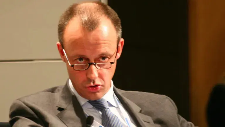 Friedrich Merz sitzt und senkt den Kopf leicht beim Reden, während er über seine Brillengläser schaut..
