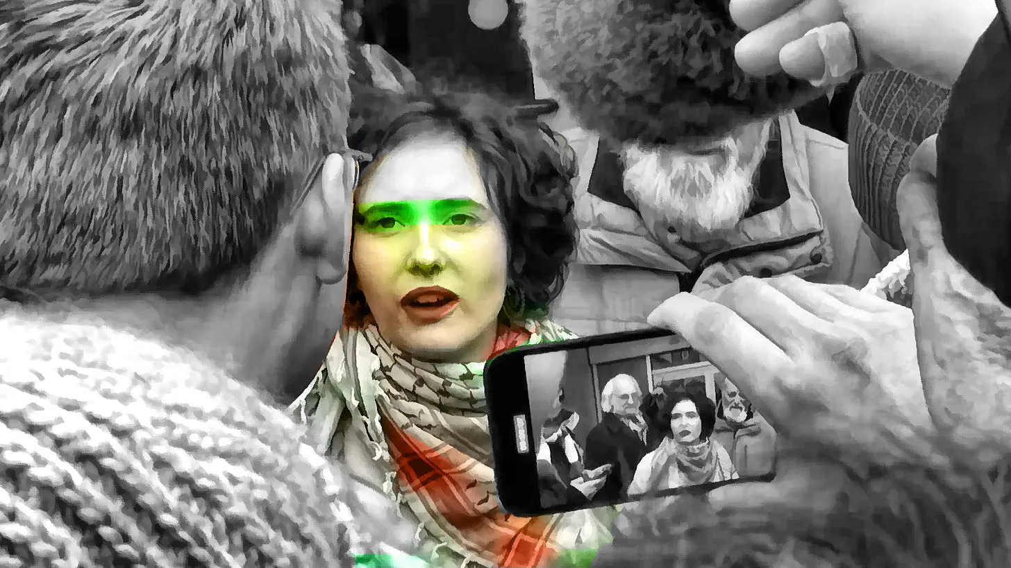 Eine Sprecherin des Palästinakommitee FU Berlin umgeben von Journalist:innen auf einer Demonstration am Donnerstag vor der FU Berlin. Das bild ist schwarz-weiß, aber ihr Gesicht und die Kufiya die sie trägt sind rot und grün eingefärbt.