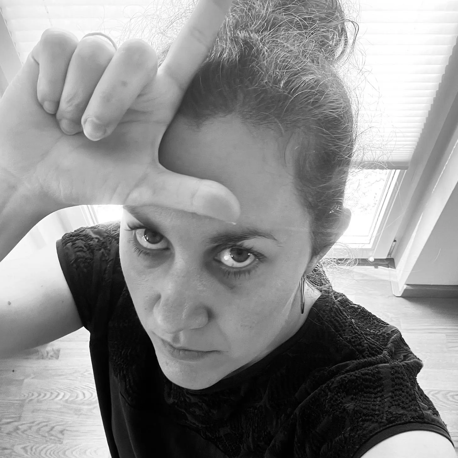 Selfie. Miriam schaut in die Kamera und hält ihre Finger wie ein L geformt über ihrer Stirn.