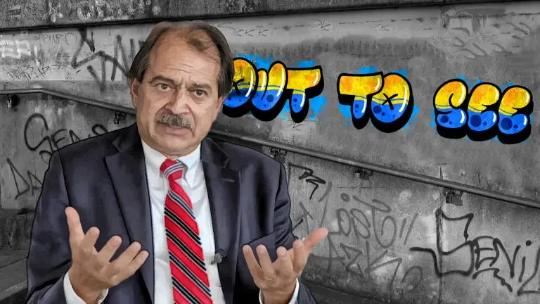 John Ioannidis vor einer Wand auf der in blau-gelber Schrift OUT TO SEE steht.