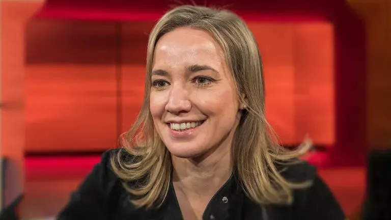 Kristina Schröder lächelt vor einem rötlichen Fernsehstudiohintergrund.