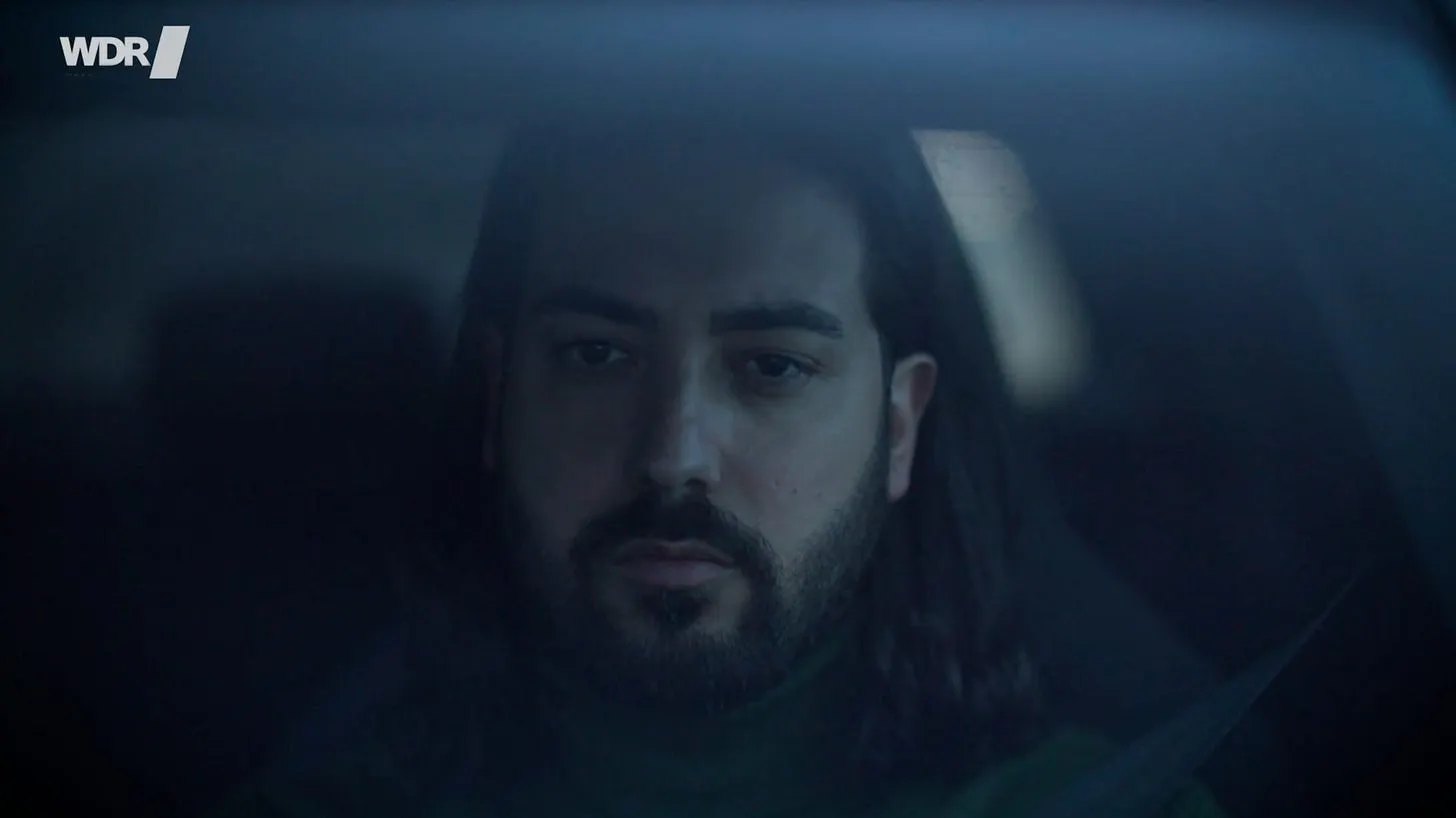 Mirza Odabaşı sitzt am Steuer seines Autos. Screenshot aus dem Film