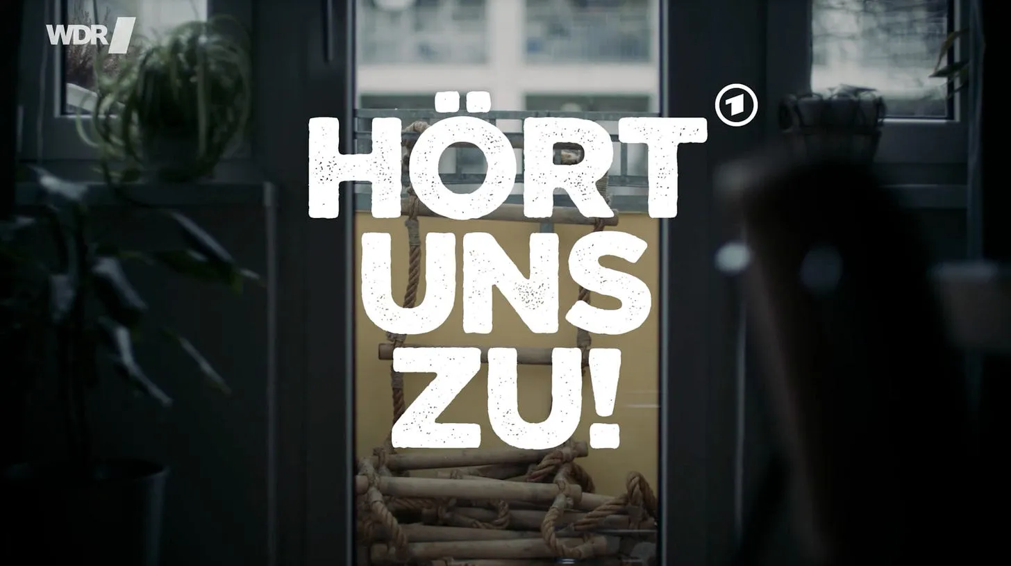 Titelbild von Hört uns zu: Im Hintergrund abgedunkelt den Blick von einem Wohnzimmer auf einen Balkon durch eine Glastür. Auf dem Balkon liegt eine Strickleiter, deren einer Teil über die Brüstung geworfen ist. Darüber drei Worte in großen weißen Buchstaben und drei Reihen: Hört uns zu!