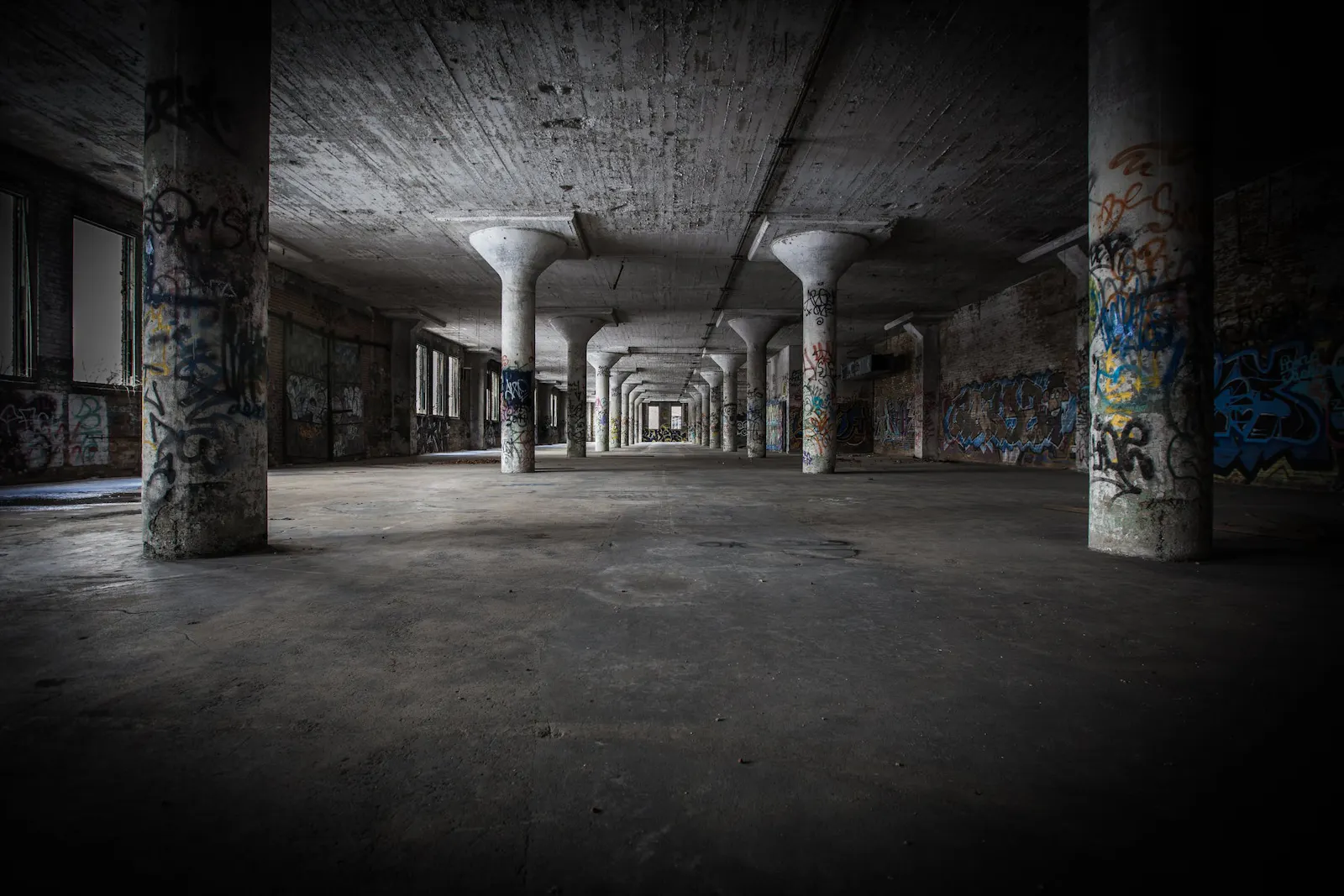 Interior black and white photo of an empty, abandoned warehouse with walls and columns covered with graffiti.