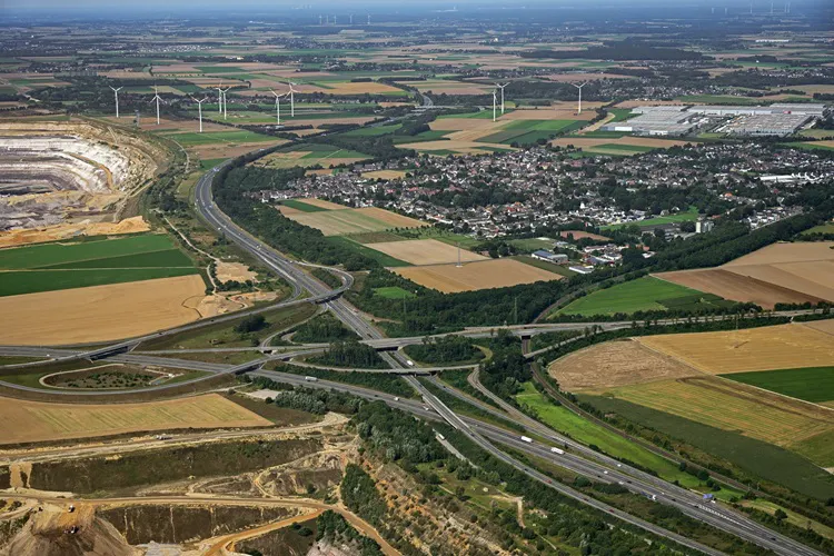 Autobahnkreuz aus der Vogelperspektive. Ringsherum Felder und in der Nähe eine Kleinstadt.