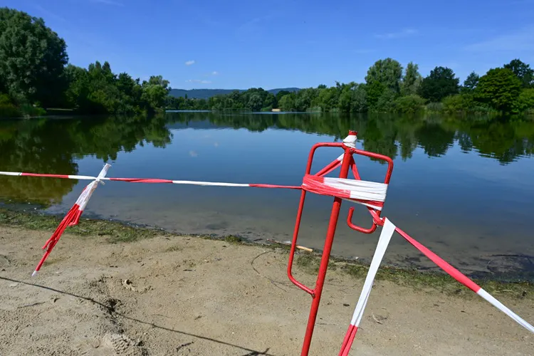 Mit rot-weißem Flatterband abgesperrtes Seeufer beii blauem Himmel und Sonnenschein.