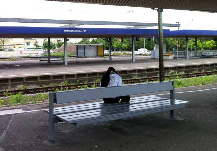 Sehr trister Bahnnhof. Eine Frau sitzt allein auf einer Bank und wartet auf ihren Zug.